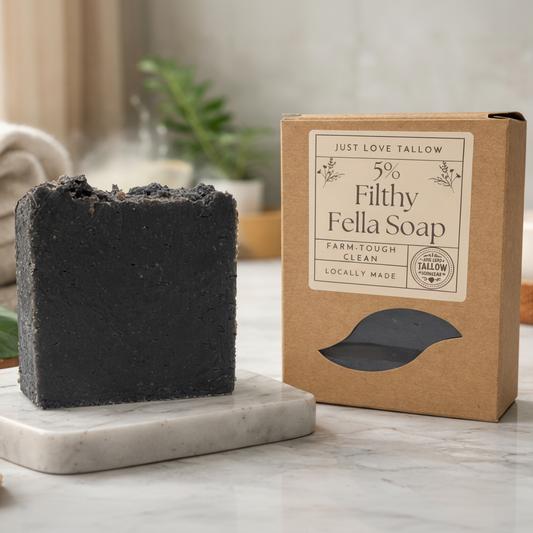 Black soap bar on a marble stand with a cardboard box labeled '5% Filthy Fella Soap' in the background.
