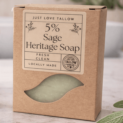 Bar of soap on a wooden soap dish with leaves and towels in the background
