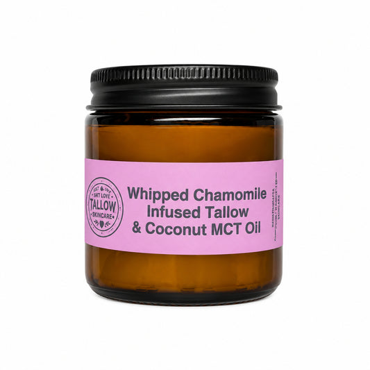 An amber glass jar with a black screw cap and a pink label reading 'Whipped Chamomile Infused Tallow & Coconut MCT Oil', set against a white fabric backdrop.