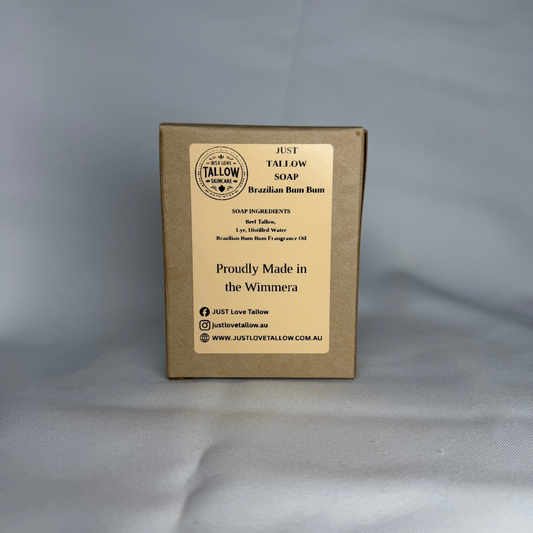 A square kraft paper box of Just Tallow Soap Brazilian Bum Balm, featuring a cream-colored label with black text, set against a light gray fabric background.