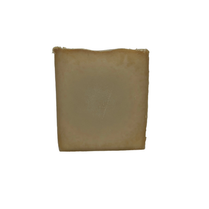 A rectangular bar of handmade soap in a warm tan or light brown color, standing upright against a white fabric backdrop.