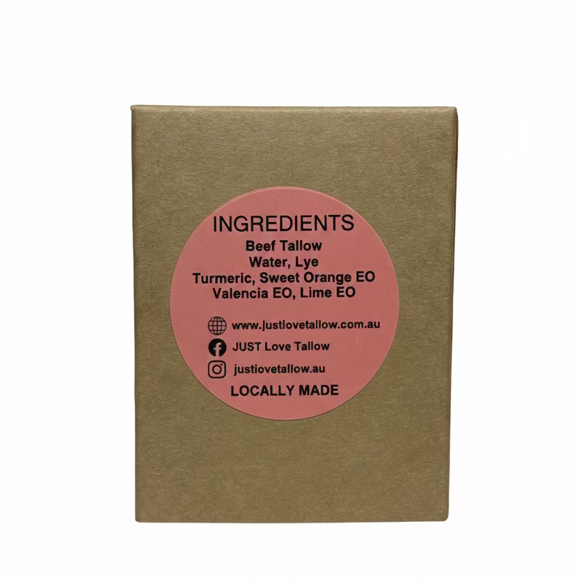 A square brown kraft paper box with a circular pink label on the front, photographed against a light gray fabric backdrop. The label reads 'INGREDIENTS' and lists natural tallow, lye, turmeric, sweet orange EO, and lima EO, with the brand name justlovetailow visible.