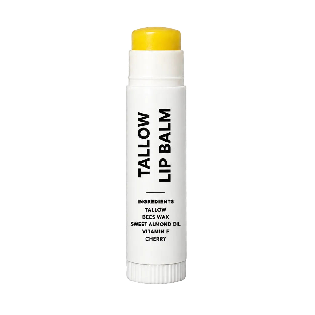 A white lip balm stick with a bright yellow cap, featuring black text that reads 'TALLOW LIP BALM' and listing ingredients including bees wax, almond oil, vitamin E, and cherry. The product is shown on a gray and white checkered background.