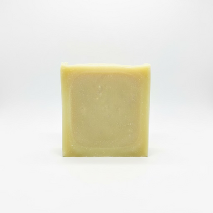 A single rectangular bar of pale yellow soap with rounded corners, standing upright against a light gray fabric background.